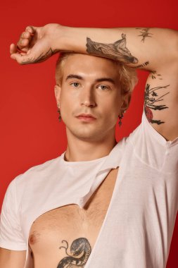 Modaya uygun bir genç, kendine güvenerek poz veriyor, dövmelerini ve benzersiz stilini canlı renklerle sergiliyor..