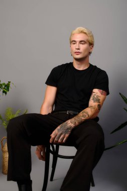 Dövmeleri olan genç yakışıklı bir adam havalı bir mekanda sakince poz veriyor ve tarzını gösteriyor..