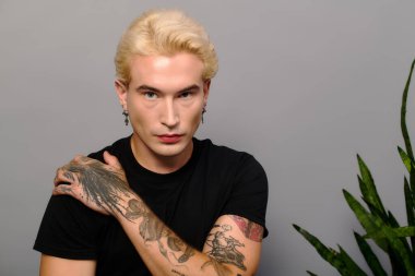 Zarif bir genç adam çekici sarı saçları ve şık dövmeleriyle cazibesini sergiliyor..