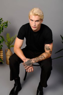 Yakışıklı genç adam kendine güvenerek oturuyor, modern tarzı ve canlı gençlik kültürünü ifade ediyor..