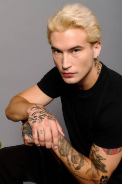 Kendine güvenen genç, tarafsız bir arkaplanda dövmeleri ve eşsiz bir stili var..