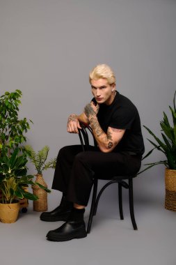 Platin saçlı genç bir adam bitkilerin arasında otururken tarzını gösteriyor..