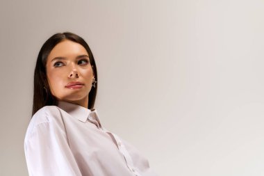 A beautiful young woman poses confidently in an elegant autumn outfit against a grey backdrop.