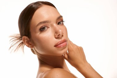 A graceful young woman poses confidently with subtle makeup against a bright backdrop.