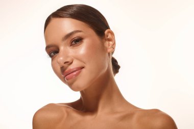 A young woman with natural makeup glows softly, her expression is warm and inviting.