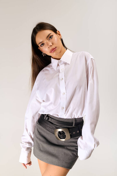 A confident young woman poses in a chic autumn outfit with a white shirt and skirt.