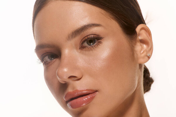 A young woman showcases her natural beauty against a white background, featuring soft makeup.