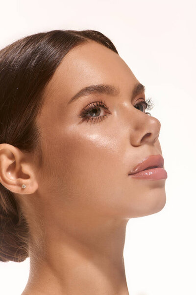 A young woman stands against a white background, highlighting her natural makeup and radiant beauty.