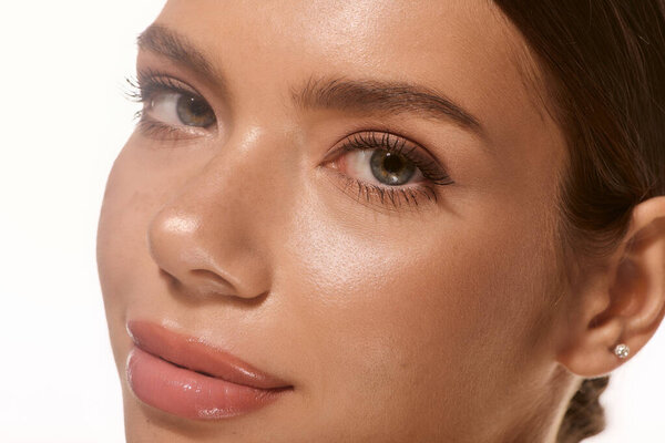 A beautiful young woman displays her natural makeup and glowing skin against a white backdrop.