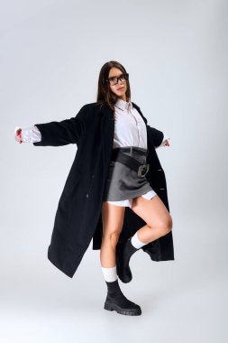 Model showcases a trendy autumn outfit featuring a white shirt and skirt in a modern studio.