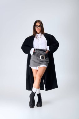 A beautiful young woman poses confidently in a trendy autumn outfit in a neutral studio.