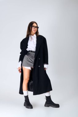 A confident young woman models a chic autumn outfit with a white shirt and skirt.
