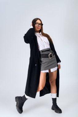 A confident young woman in a chic autumn outfit poses in grey.