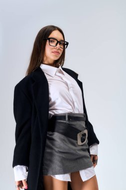 A young woman confidently poses in a chic white shirt and skirt, embracing autumn vibes in a studio.