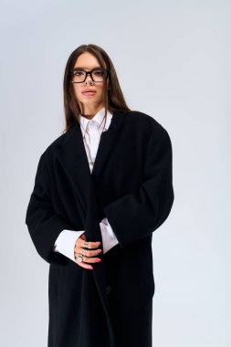 A beautiful young woman showcases a trendy autumn outfit in a grey studio, radiating elegance.