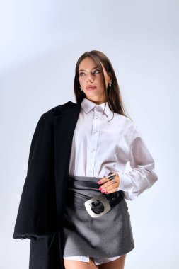 A young woman poses confidently in a chic autumn outfit with a white shirt and grey skirt.
