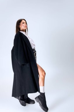 A young woman poses confidently in a chic autumn outfit with a white shirt and skirt.