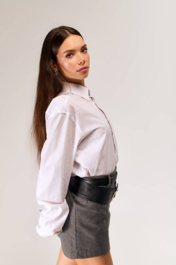 A young woman poses elegantly in a stylish autumn outfit with a white shirt and skirt.