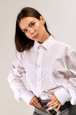 A beautiful young woman poses confidently in a stylish autumn outfit against a grey background.