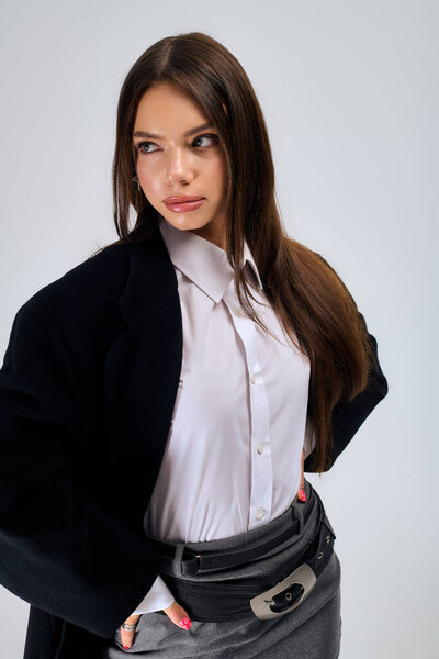 A beautiful young woman poses confidently in a stylish autumn outfit in a grey studio setting.