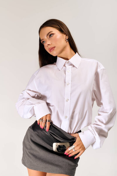 A young woman poses confidently in a trendy autumn outfit featuring a white shirt and skirt.