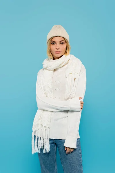 Jeune femme blonde en pull blanc et chapeau d'hiver debout isolé sur bleu — Photo de stock