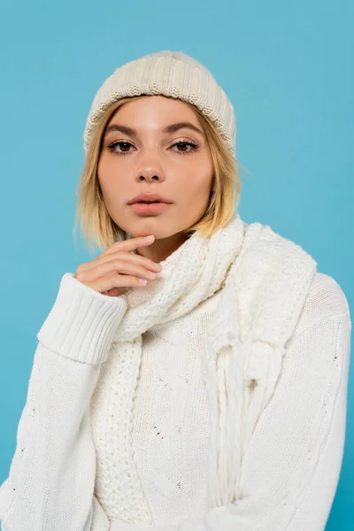 Portrait de jeune femme blonde en pull blanc, écharpe d'hiver et bonnet tricoté isolé sur bleu — Photo de stock