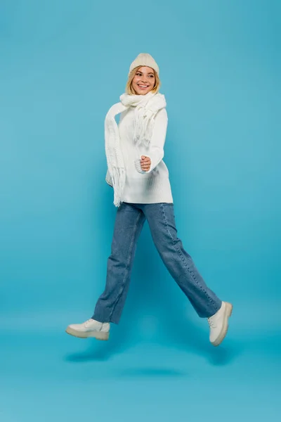 Comprimento total de feliz jovem mulher em roupa de inverno levitando em azul — Fotografia de Stock