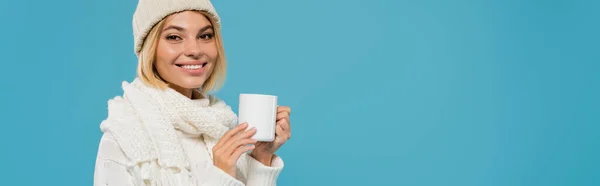 Cheerful woman in white sweater and hat holding cup of coffee isolated on blue, banner — Stock Photo