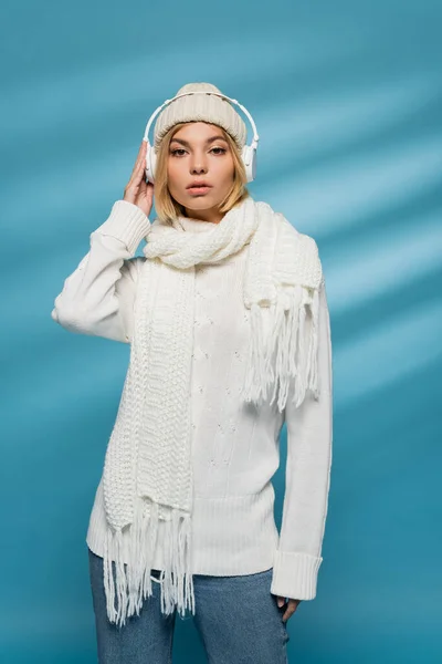 Stylische junge Frau im Winteroutfit und kabellosen Kopfhörern, die Musik auf blau hören — Stockfoto