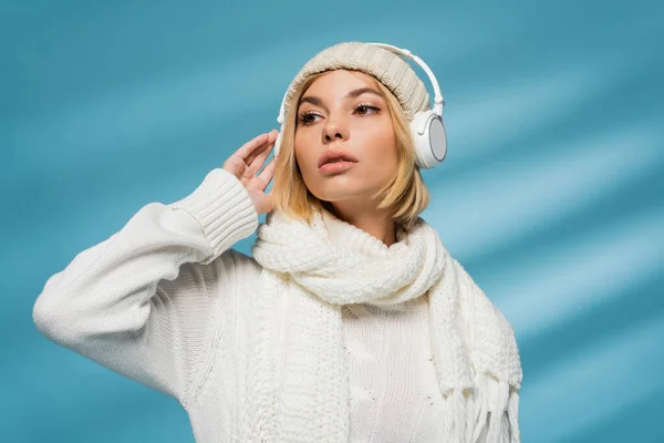 Young woman in white winter outfit and wireless headphones listening music on blue — Stock Photo