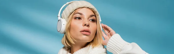 Stylish young woman in winter outfit and wireless headphones listening music on blue, banner — Stock Photo