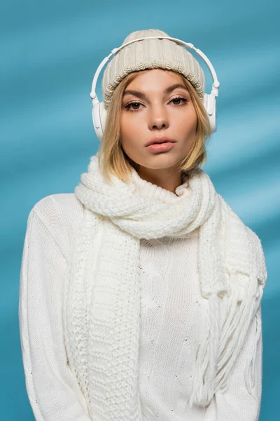 Blonde woman in winter hat and wireless headphones listening music on blue — Stock Photo