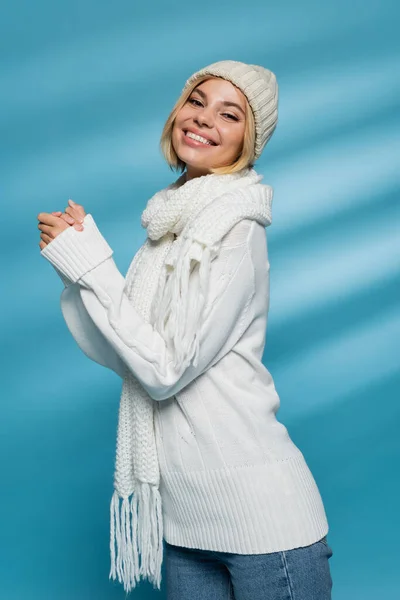 Happy young woman in knitted hat and winter sweater smiling on blue — Stock Photo