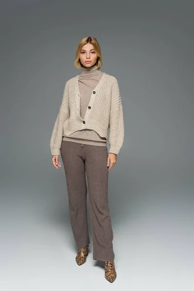 Full length of young woman in turtleneck and cardigan standing on grey — Stock Photo