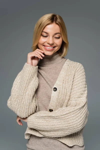 Cheerful blonde woman in turtleneck and cardigan smiling isolated on grey — Stock Photo