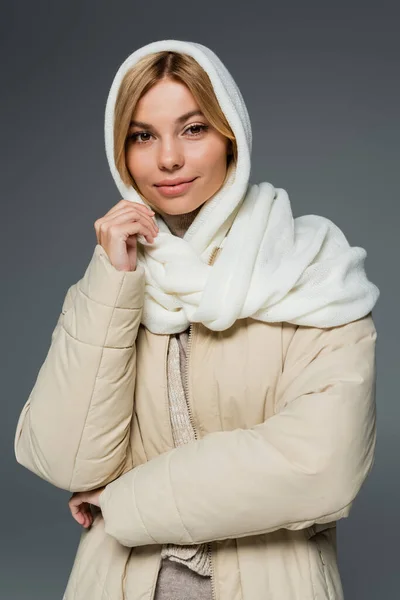 Mujer joven con estilo en invierno pañuelo para la cabeza y chaqueta hinchable mirando a la cámara aislada en gris - foto de stock