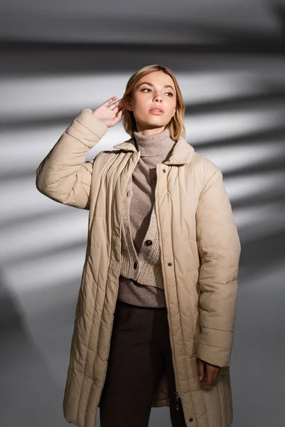 Mujer con estilo en traje de invierno tocando el pelo sobre fondo gris abstracto - foto de stock