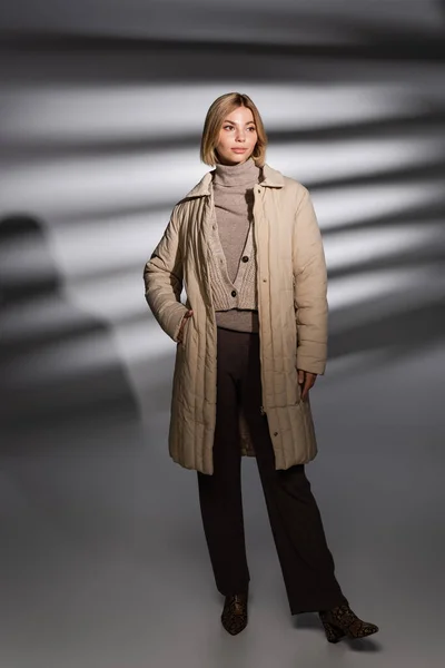 Volle Länge der stilvollen Frau in Winterjacke posiert auf abstraktem grauen Hintergrund — Stockfoto