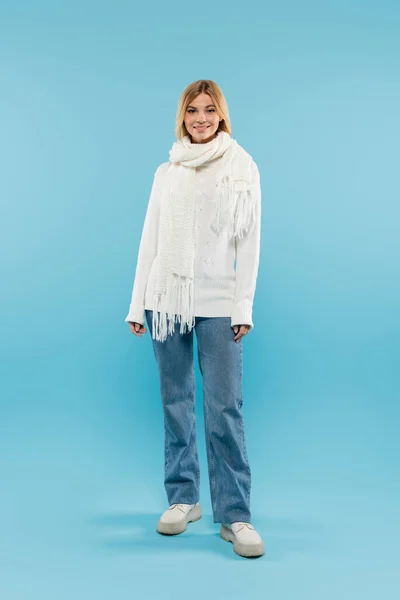 Full length of pretty blonde woman in sweater and jeans looking at camera on blue background — Stock Photo