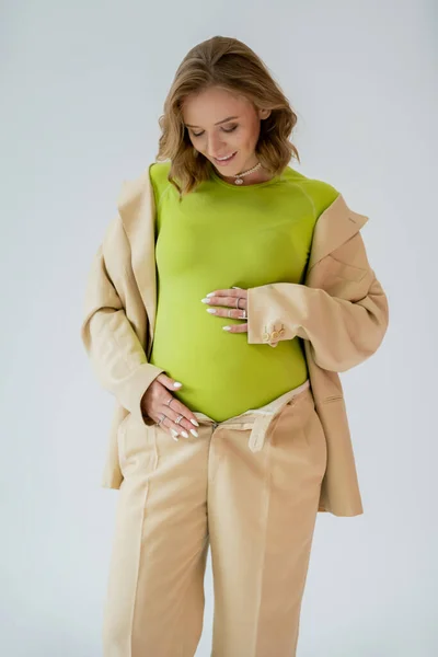 Femme enceinte positive en costume touchant le ventre isolé sur gris — Photo de stock