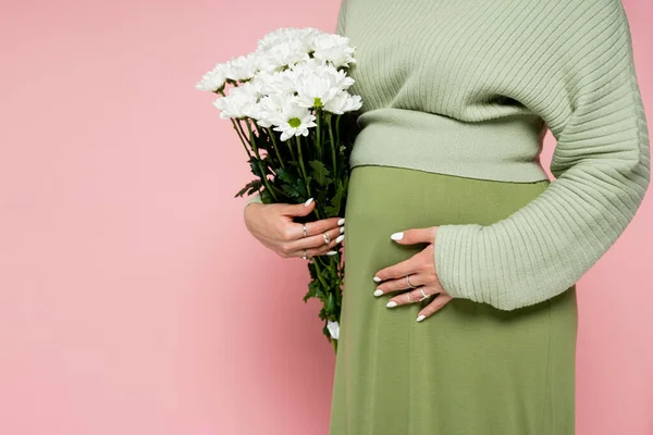 Vista recortada de la mujer embarazada en suéter sosteniendo flores aisladas en rosa - foto de stock