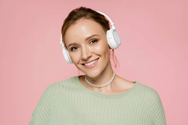 Cheerful woman in green sweater and headphones looking at camera isolated on pink — Stock Photo