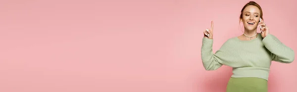 Положительная беременная женщина разговаривает на смартфоне и указывает пальцем на розовый фон, баннер — стоковое фото