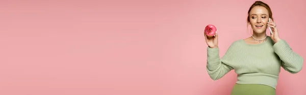 Mulher grávida feliz falando no smartphone e olhando para donut doce isolado em rosa, banner — Fotografia de Stock