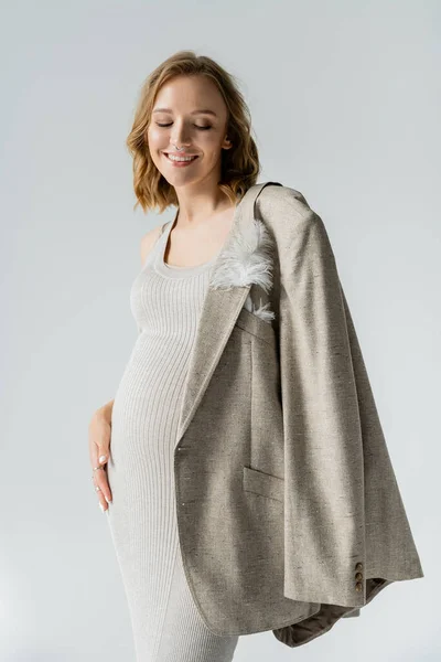 Stilvolle schwangere Frau im Kleid blickt auf Jacke mit Feder isoliert auf grau — Stockfoto