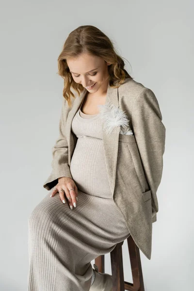 Mulher grávida feliz no vestido sentado na cadeira isolada no cinza — Fotografia de Stock