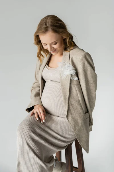 Happy pregnant woman in dress sitting on chair isolated on grey — Stock Photo