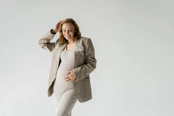 Joyeux femme enceinte en robe et veste posant isolé sur gris — Photo de stock