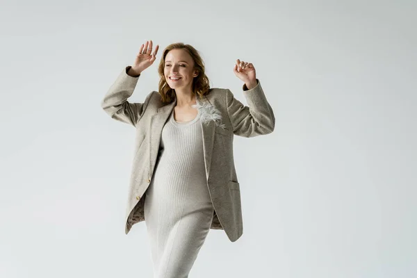 Allegro donna incinta in abito e giacca mano ondulante isolato su grigio — Foto stock